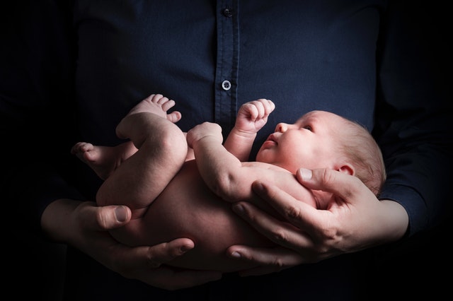 Muž v modrej košeli drží na rukách nahého novorodenca