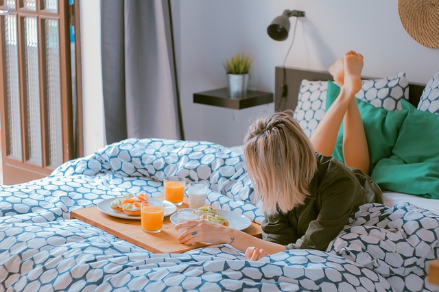 Žena leží na posteli s farebnými vzorovanými obliečkami a má pri sebe raňajky.jpg