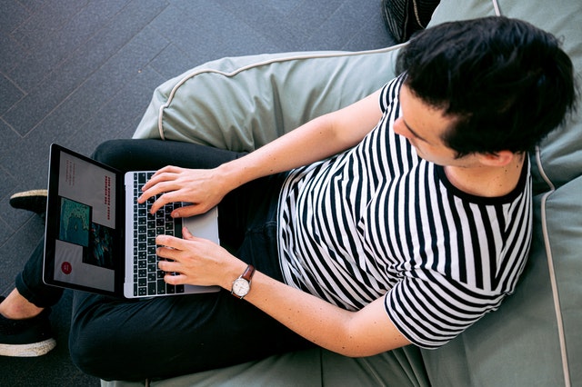 Muž v pásikavom tričku sedí na gauči a pracuje na notebooku